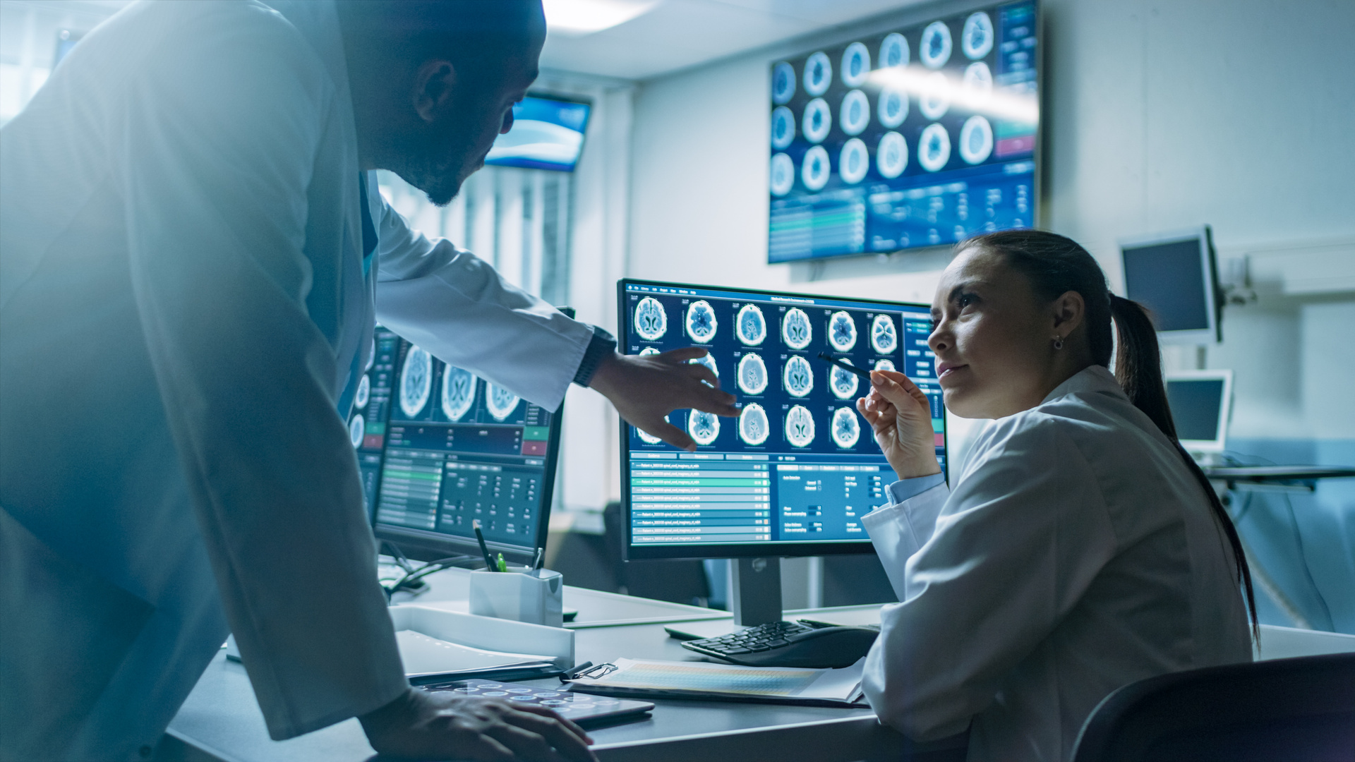 Two Scientists In The Brain Research Laboratory Work On A Project, Using Personal Computer With Mri Scans Show Brain Anomalies. Neuroscientists At Work.